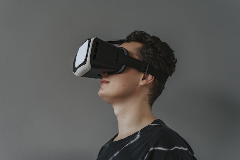 A close-up image of a man wearing a black VR headset against a gray background.