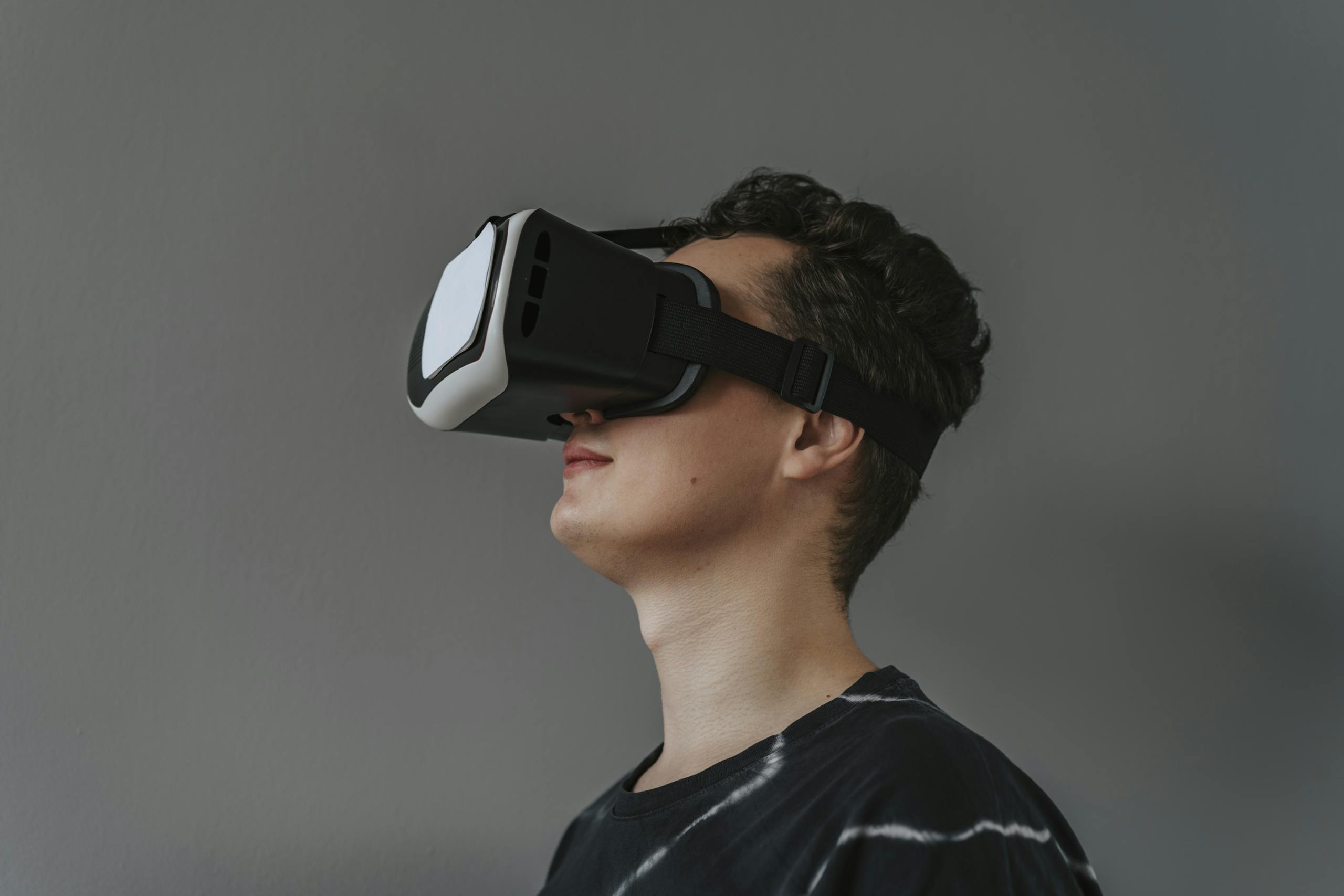 A close-up image of a man wearing a black VR headset against a gray background.