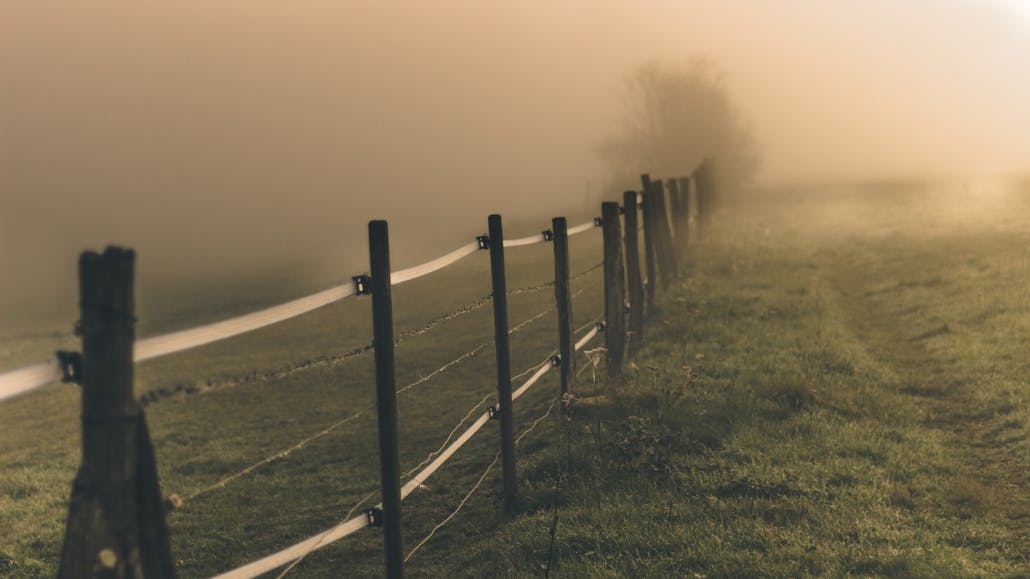 Tranquil countryside scene with a fence leading into the misty, fog-filled horizon.